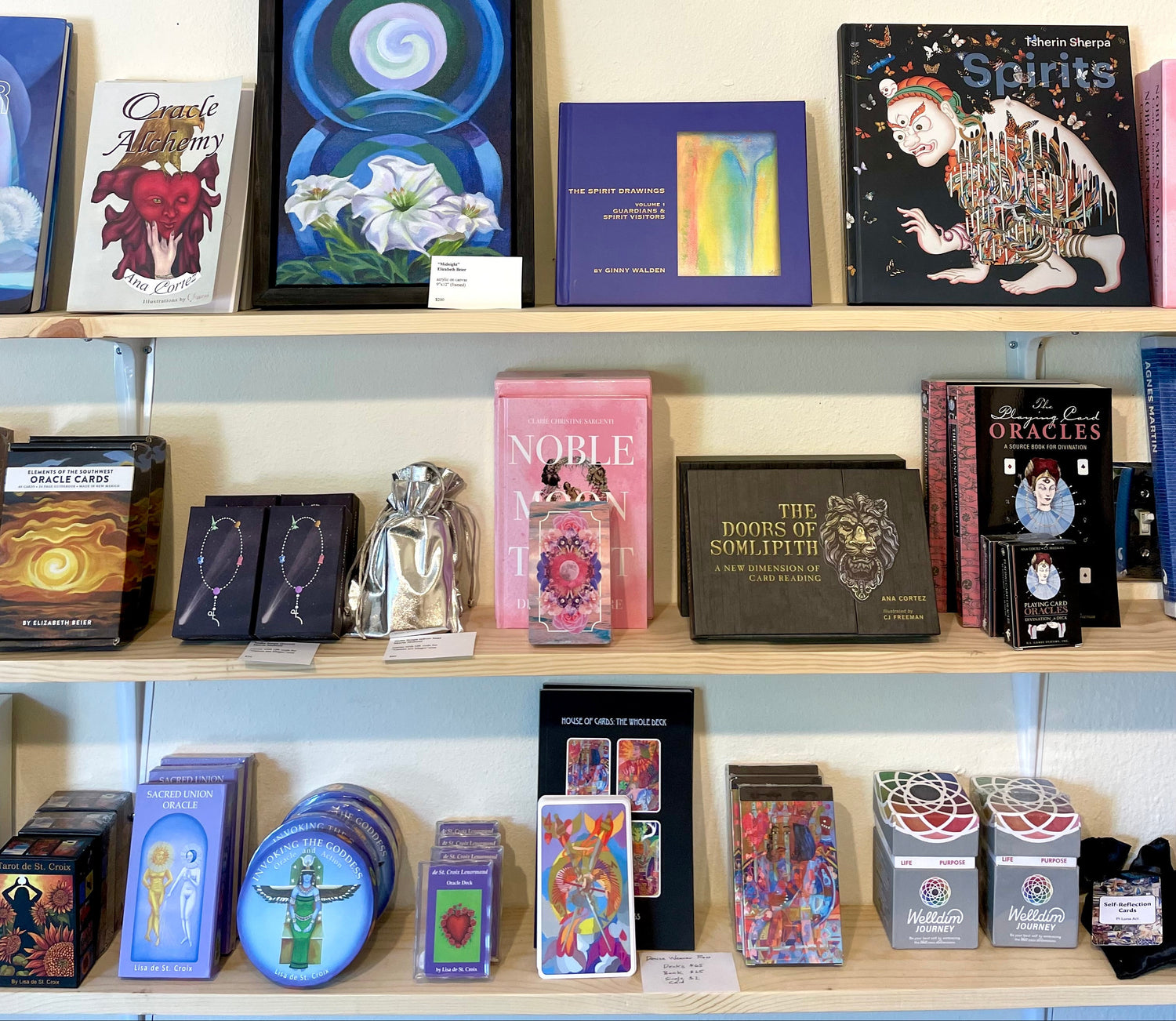 Shelf displaying various books, tarot cards, and artwork in a store setting.
